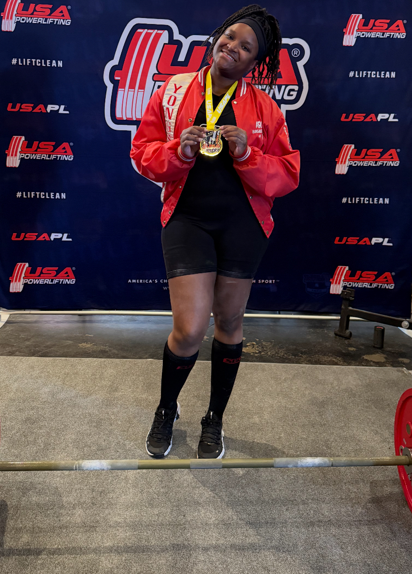 Sherita Ariola holding her first-place medal at a USA Powerlifting competition
